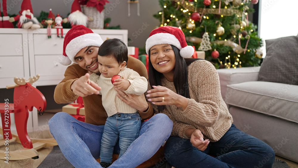 Couple and son holding decoration ball sitting on floor by christmas tree at home Couple and son holding decoration ball sitting on floor by christmas tree at home