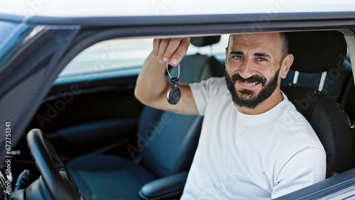 Young hispanic man smiling confident holding key of new car at street