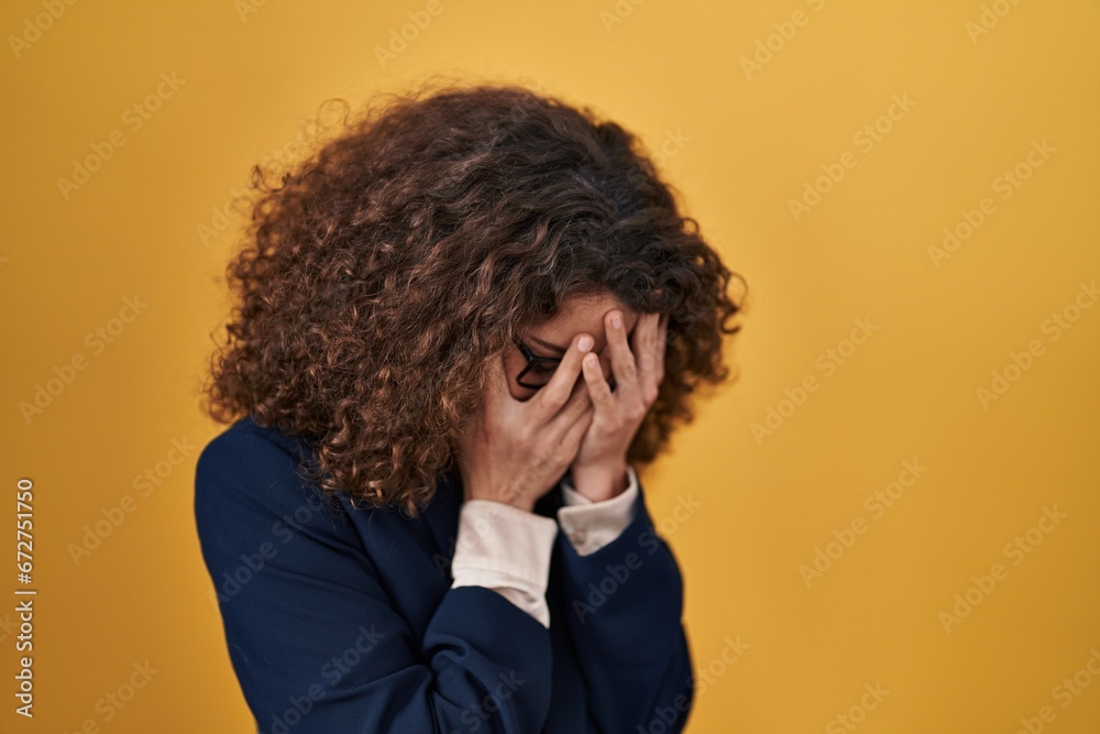 Hispanic woman with curly hair standing over yellow background with sad expression covering face with hands while crying. depression concept. Hispanic woman with curly hair standing over yellow background with sad expression covering face with hands while crying. depression concept.