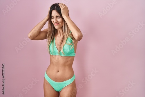 Young hispanic woman wearing bikini over pink background suffering from headache desperate and stressed because pain and migraine. hands on head.