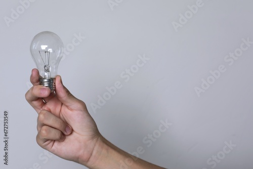 Hand holds light bulb on white background. Demonstrates energy savings, copy space