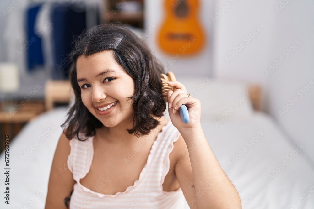 Young woman combing hair sitting on bed at bedroom Young woman combing hair sitting on bed at bedroom