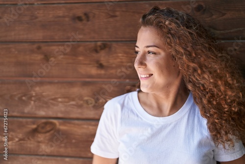 Young beautiful hispanic woman smiling confident looking to the side over isolated wooden background