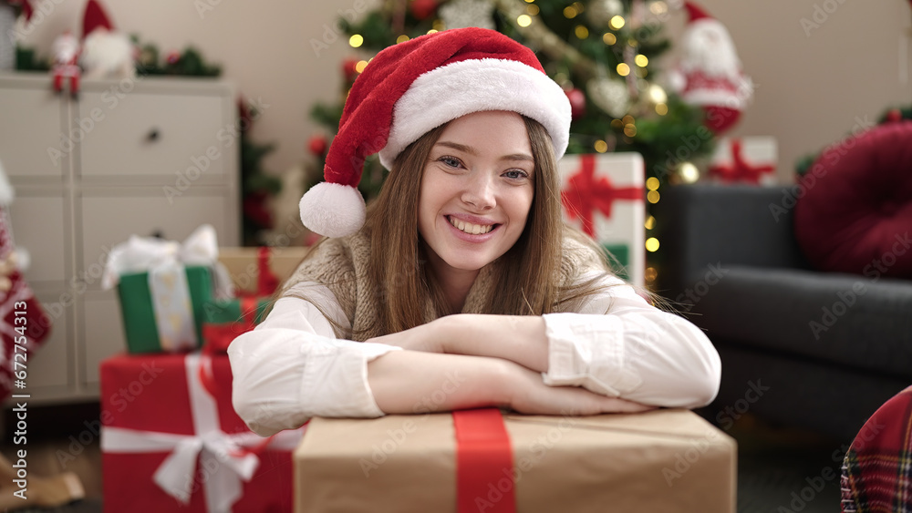 Young blonde woman sitting by christmas tree leaning on gift at home Young blonde woman sitting by christmas tree leaning on gift at home