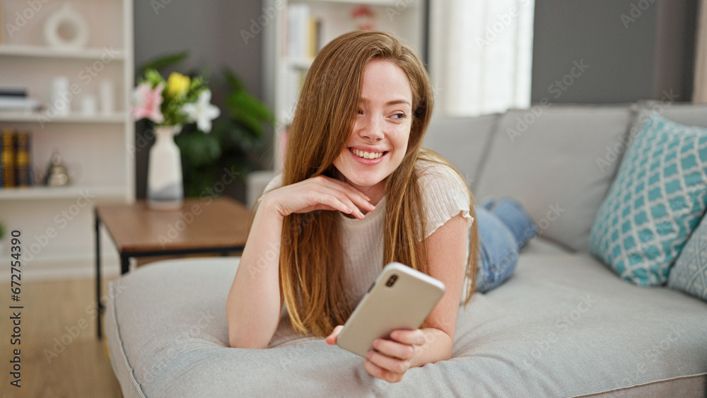 Young blonde woman using smartphone lying on sofa at home