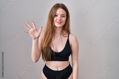 Young caucasian woman wearing lingerie showing and pointing up with fingers number five while smiling confident and happy. © Krakenimages.com