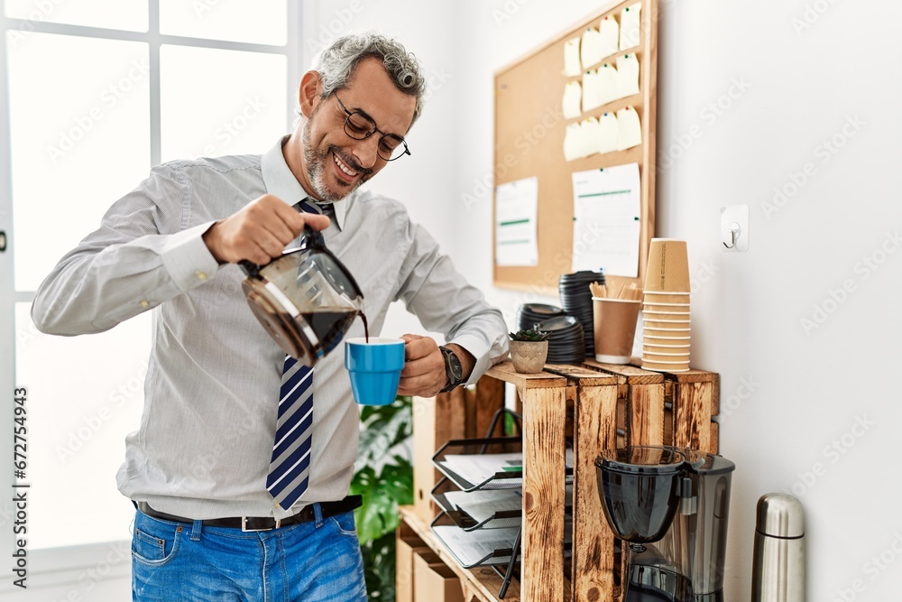 Middle age grey-haired man business worker pouring coffee on cup at office
