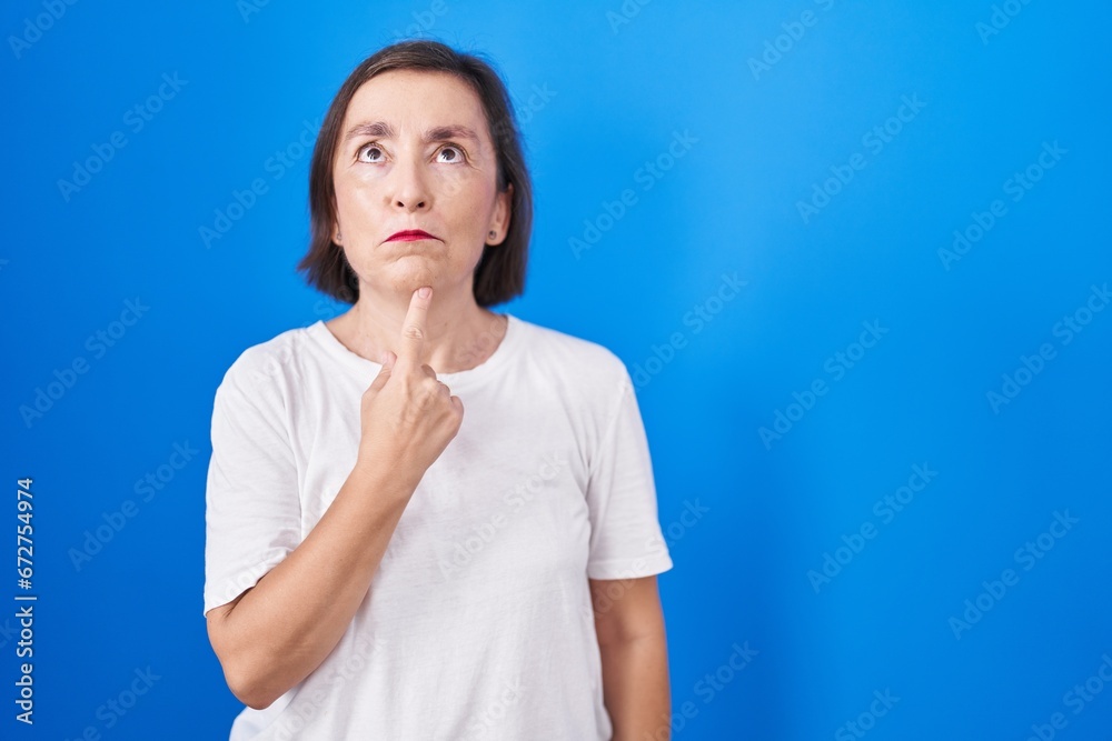 Middle age hispanic woman standing over blue background thinking concentrated about doubt with finger on chin and looking up wondering Middle age hispanic woman standing over blue background thinking concentrated about doubt with finger on chin and looking up wondering