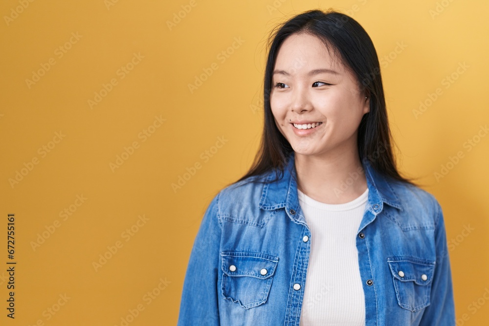 Young asian woman standing over yellow background looking away to side with smile on face, natural expression. laughing confident. Young asian woman standing over yellow background looking away to side with smile on face, natural expression. laughing confident.