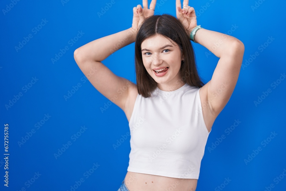 Young caucasian woman standing over blue background posing funny and crazy with fingers on head as bunny ears, smiling cheerful