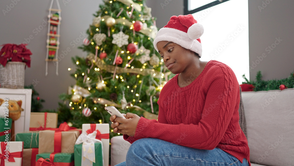 African american woman celebrating christmas using smartphone at home African american woman celebrating christmas using smartphone at home