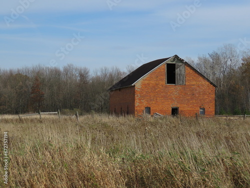 Old Rustic Dilapidated Orange Brick Barn in Autumn Field against Background of Bare Trees and Blue Sky with Wispy Clouds on November Day in Michigan