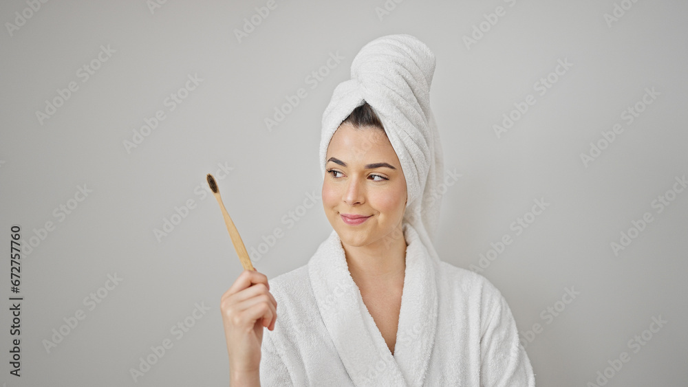 Young beautiful hispanic woman wearing bathrobe holding toothbrush over isolated white background Young beautiful hispanic woman wearing bathrobe holding toothbrush over isolated white background