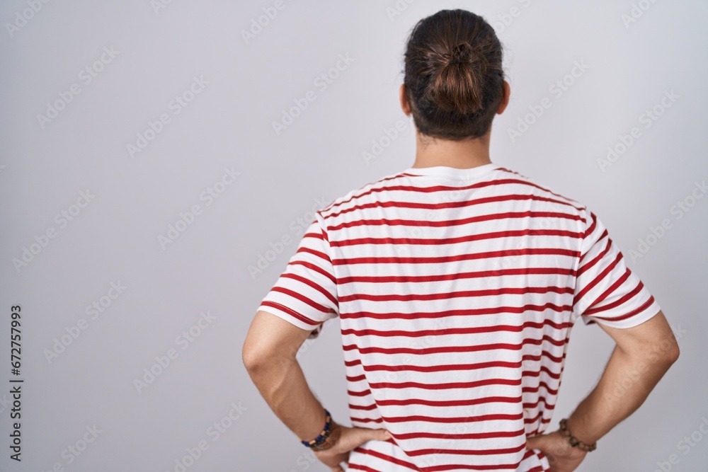 Hispanic man with long hair standing over isolated background standing backwards looking away with arms on body
