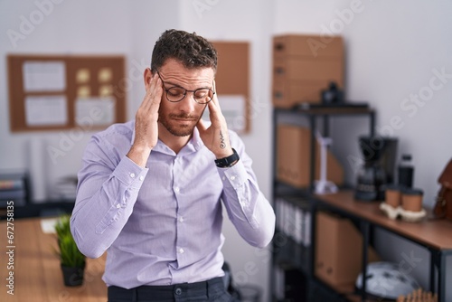 Young hispanic man at the office with hand on head, headache because stress. suffering migraine.
