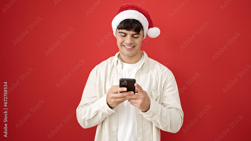 Young hispanic man wearing christmas hat using smartphone over isolated red background Young hispanic man wearing christmas hat using smartphone over isolated red background