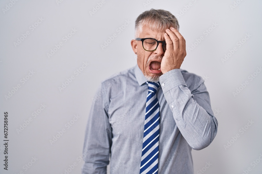 Hispanic business man with grey hair wearing glasses yawning tired covering half face, eye and mouth with hand. face hurts in pain. Hispanic business man with grey hair wearing glasses yawning tired covering half face, eye and mouth with hand. face hurts in pain.