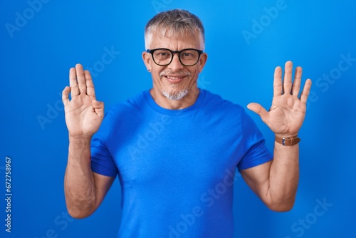 Hispanic man with grey hair standing over blue background showing and pointing up with fingers number nine while smiling confident and happy.
