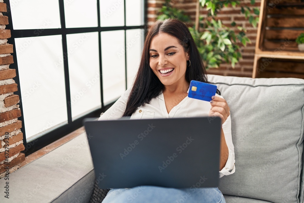 Young beautiful hispanic woman using laptop and credit card sitting on sofa at home Young beautiful hispanic woman using laptop and credit card sitting on sofa at home