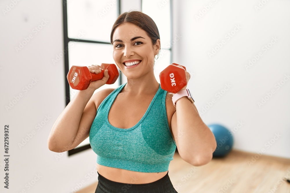 Young beautiful hispanic woman smiling confident using dumbbells training at sport center Young beautiful hispanic woman smiling confident using dumbbells training at sport center