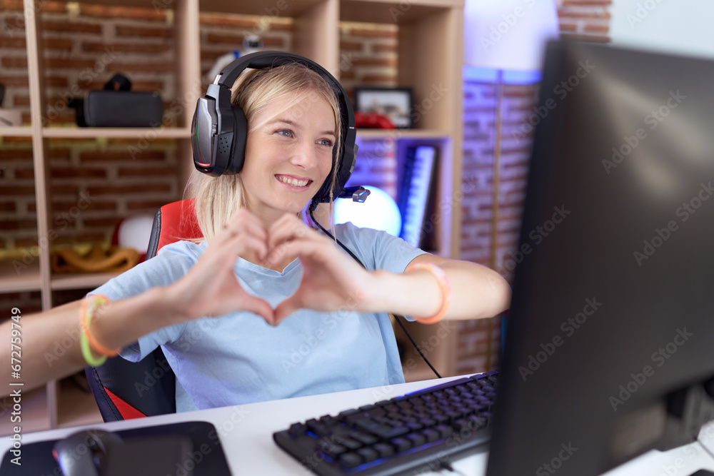 Young caucasian woman playing video games wearing headphones smiling in love doing heart symbol shape with hands. romantic concept. Young caucasian woman playing video games wearing headphones smiling in love doing heart symbol shape with hands. romantic concept.
