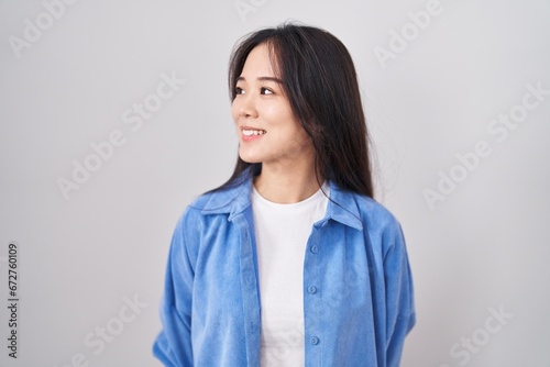 Young chinese woman standing over white background looking away to side with smile on face, natural expression. laughing confident. photo