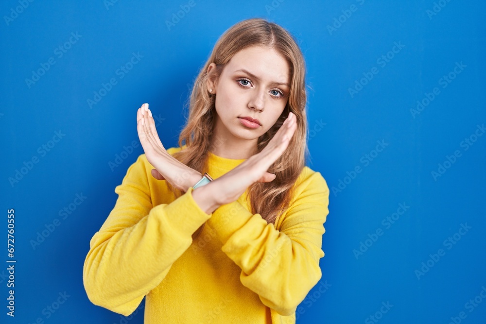 Young caucasian woman standing over blue background rejection expression crossing arms doing negative sign, angry face Young caucasian woman standing over blue background rejection expression crossing arms doing negative sign, angry face