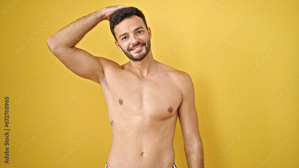 Young hispanic man tourist standing shirtless touching head over isolated yellow background