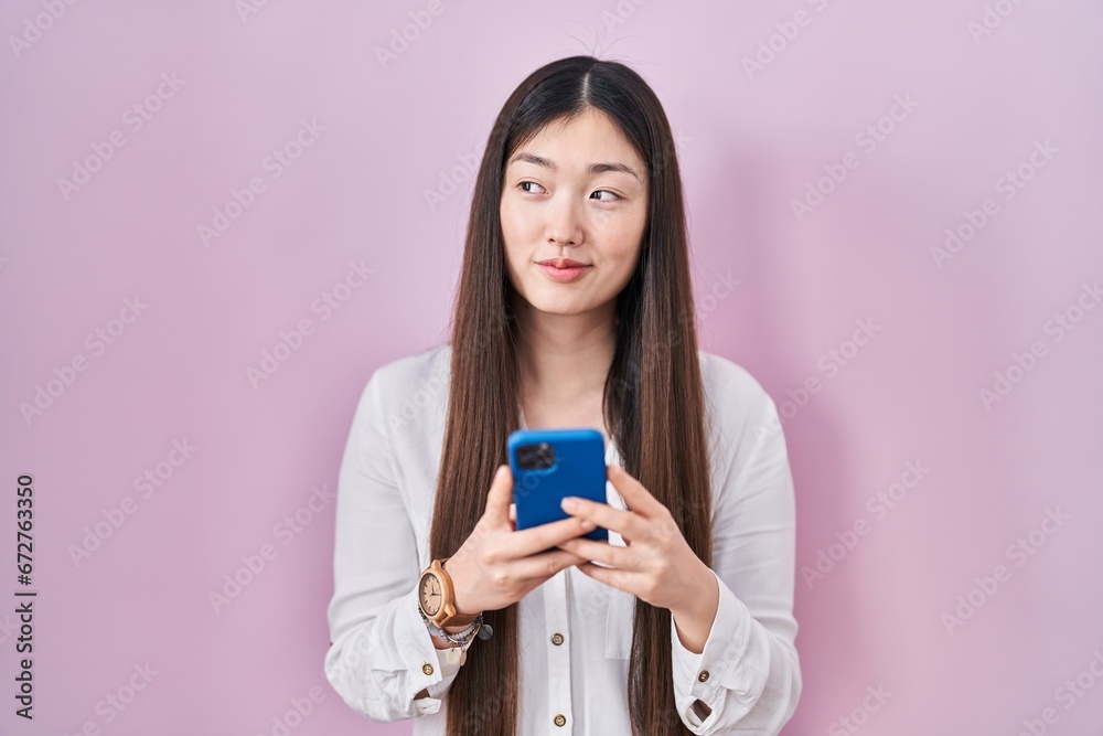 Chinese young woman using smartphone typing message smiling looking to the side and staring away thinking. Chinese young woman using smartphone typing message smiling looking to the side and staring away thinking.