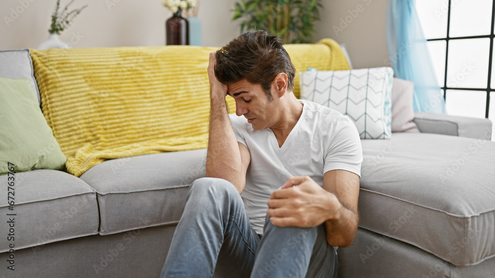 Young hispanic man stressed sitting on floor at home
