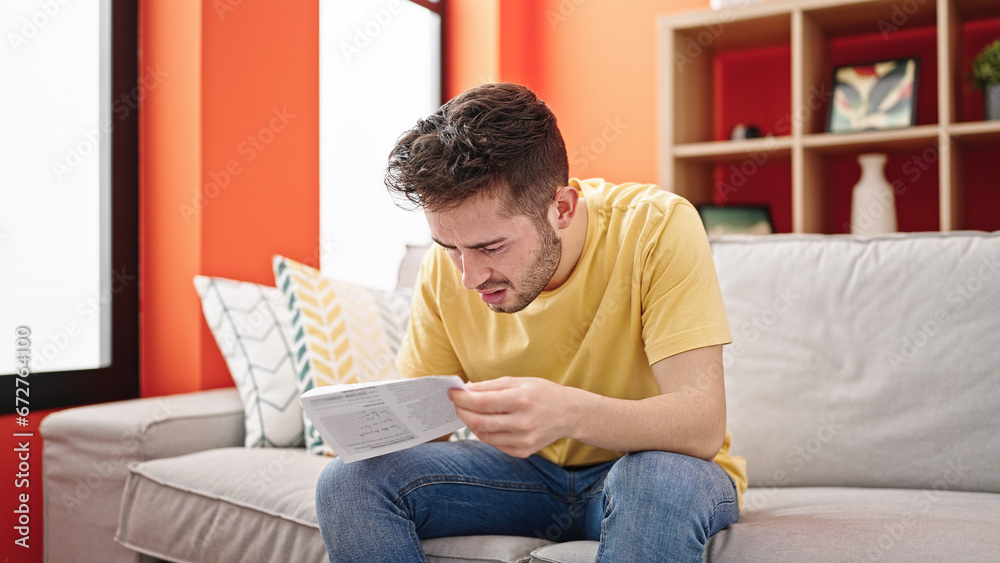 Young hispanic man reading document sitting on the sofa at home
