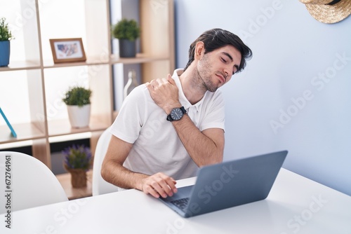 Young hispanic man using laptop suffering for bachache at home photo
