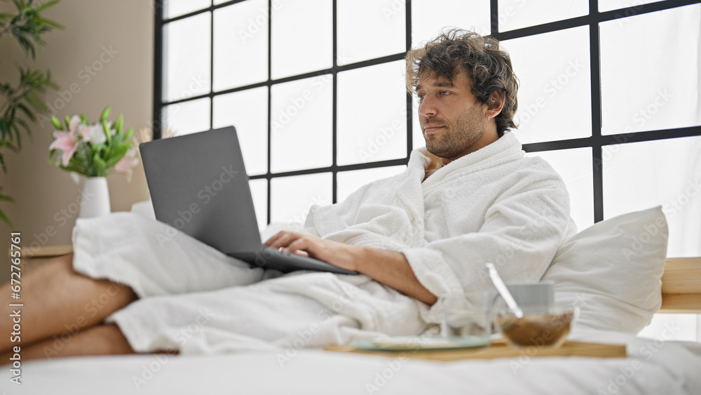Young hispanic man wearing bathrobe using laptop at bedroom Young hispanic man wearing bathrobe using laptop at bedroom