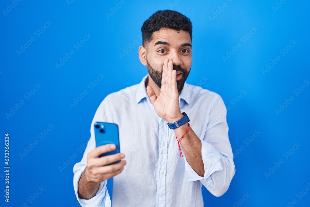 Hispanic man with beard using smartphone typing message hand on mouth telling secret rumor, whispering malicious talk conversation Hispanic man with beard using smartphone typing message hand on mouth telling secret rumor, whispering malicious talk conversation