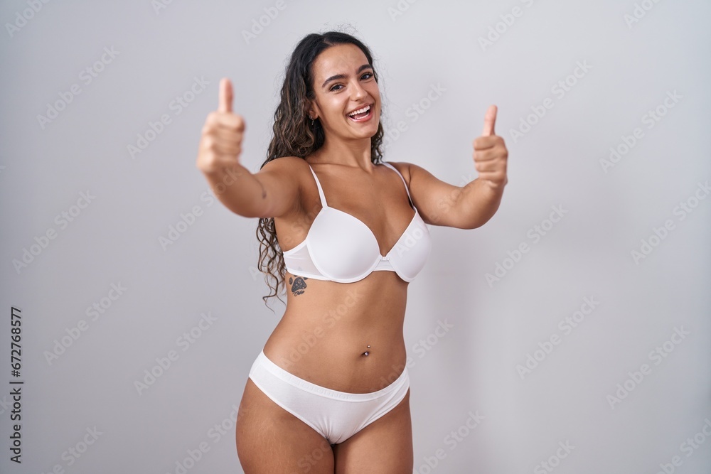 Young hispanic woman wearing white lingerie approving doing positive gesture with hand, thumbs up smiling and happy for success. winner gesture. Young hispanic woman wearing white lingerie approving doing positive gesture with hand, thumbs up smiling and happy for success. winner gesture.