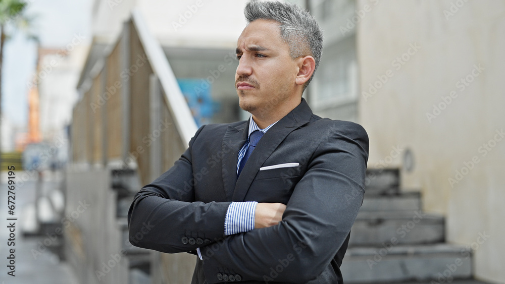 Young hispanic man business worker standing with serious face and arms crossed gesture at street Young hispanic man business worker standing with serious face and arms crossed gesture at street