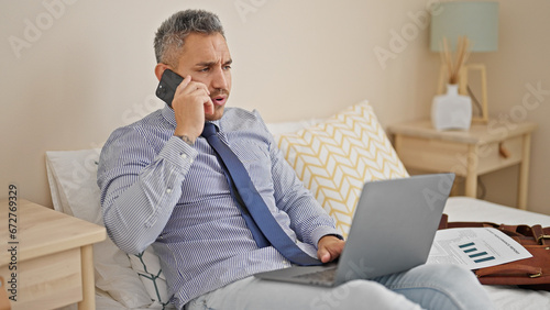 Young hispanic man business worker talking on smartphone using laptop at hotel room