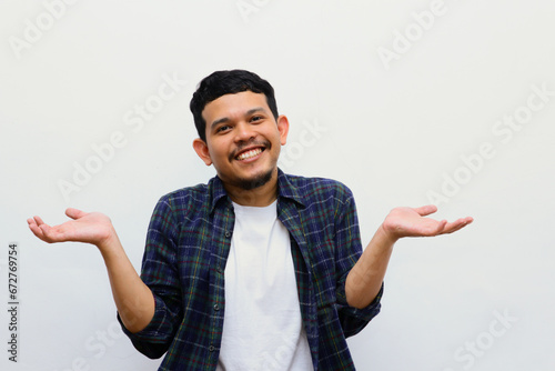 Young adult asian man raised arms and looking at camera with smiling face. studio shot, isolated on light grey background. photo