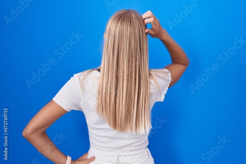 Young caucasian woman standing over blue background backwards thinking about doubt with hand on head