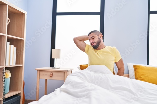 Young latin man waking up stretching arms at bedroom