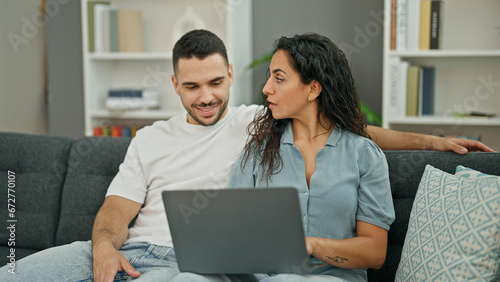 Man and woman couple using laptop sitting on sofa at home