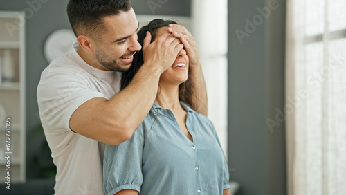 Man and woman couple surprise with hands on eyes hugging each other smiling at home