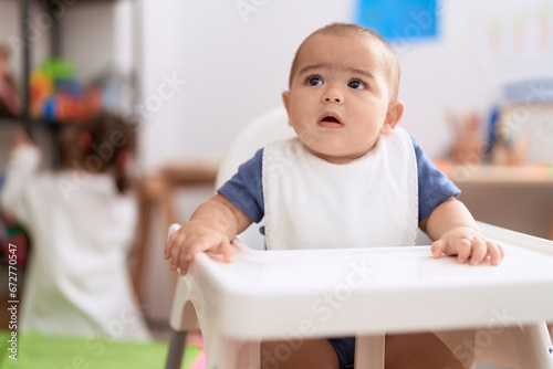 Adorable chinese toddler wearing bib sitting on dinner chair baby at home