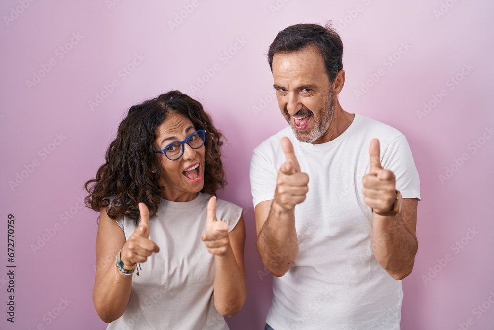 Middle age hispanic couple together over pink background pointing fingers to camera with happy and funny face. good energy and vibes. Middle age hispanic couple together over pink background pointing fingers to camera with happy and funny face. good energy and vibes.