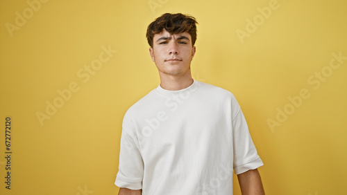 Cool young hispanic teenager guy, standing relaxed with serious expression against yellow isolated background, looking handsome in casual lifestyle portrait. © Krakenimages.com
