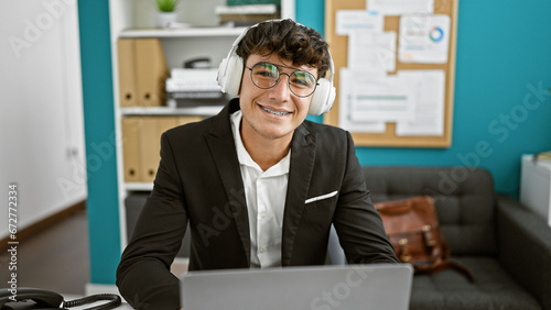Konstfotografi Young hispanic business whiz, a smiling teenager working with laptop and headpho