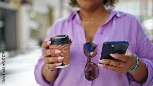 Young beautiful latin woman using smartphone holding coffee at street