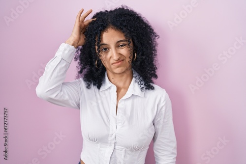 Hispanic woman with curly hair standing over pink background worried and stressed about a problem with hand on forehead, nervous and anxious for crisis