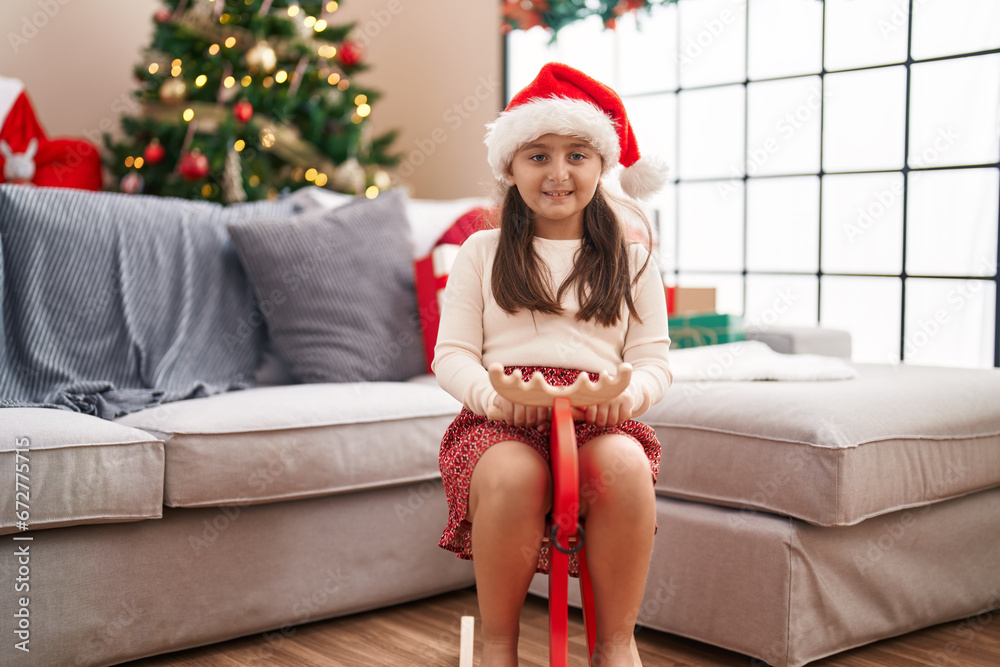 Adorable hispanic girl playing with reindeer rocking by christmas tree at home