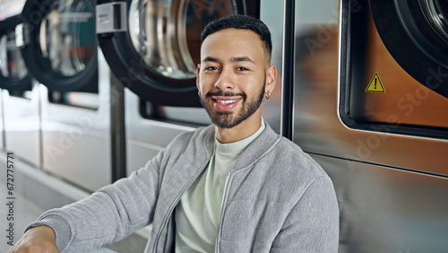 Fotografija Young hispanic man smiling confident sitting on the floor at laundry facility